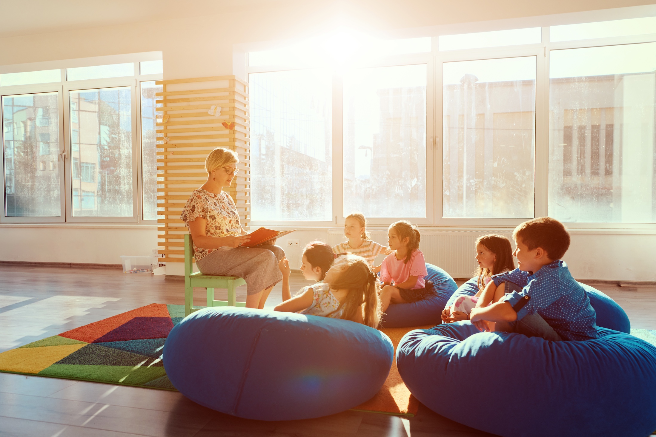 Teacher,Reading,Story,To,Children,During,Classroom,Storytime,On,Beanbags